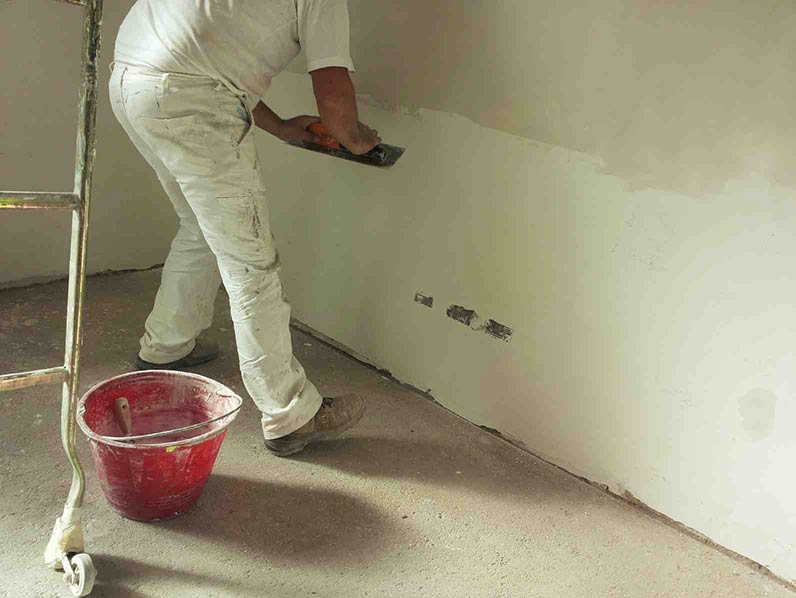 Photo d'un plâtrier qui lisse un mur au plâtre
